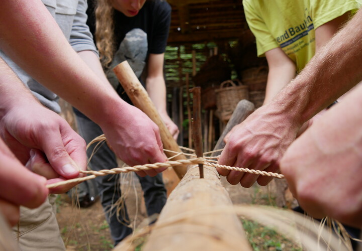 Freiwillige bearbeiten einen Stamm mit einem Stück Holz und Seil.
